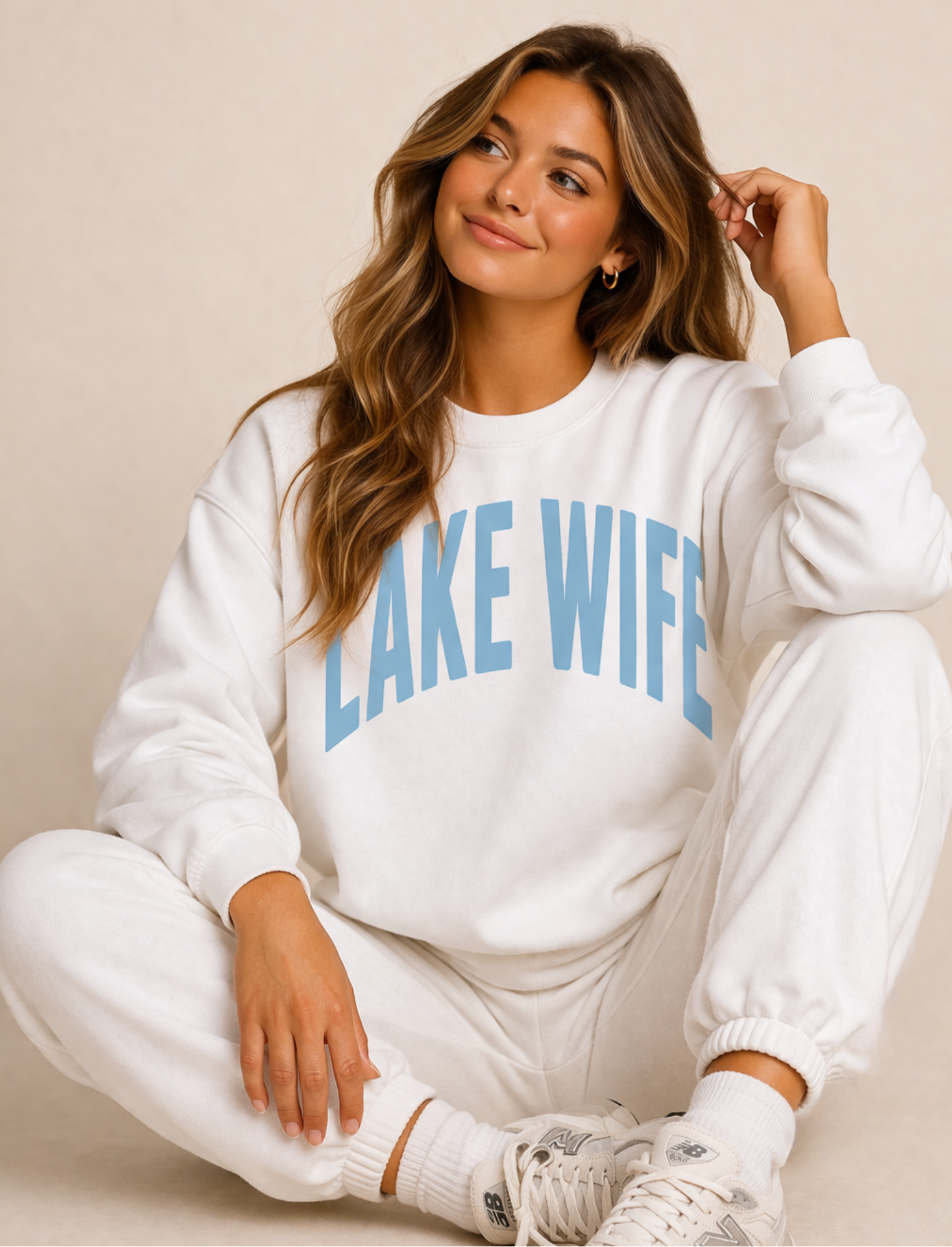 Woman wearing a white sweatshirt with 'LAKE WIFE' text on a beige background